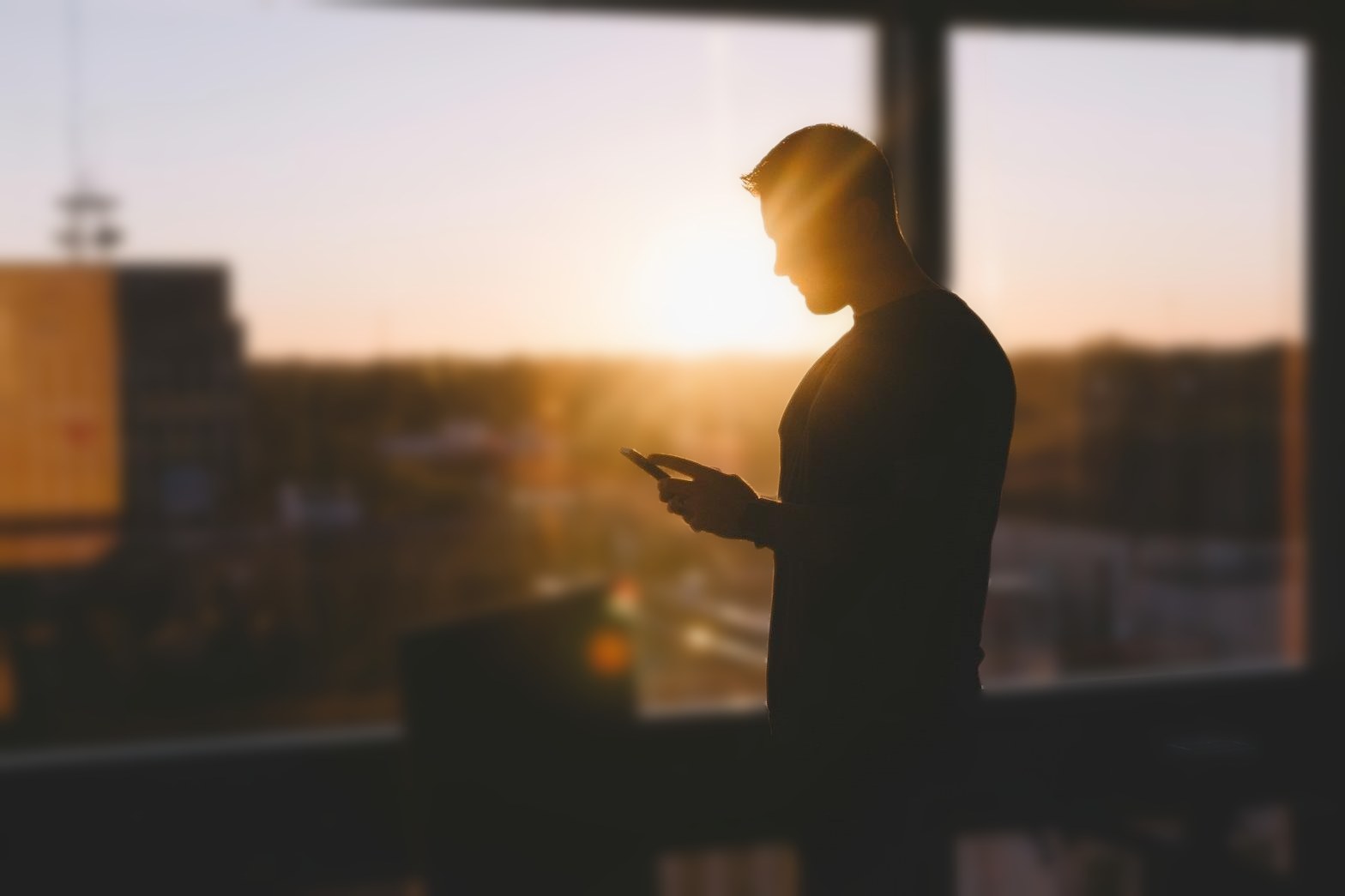 Diretor lendo uma mensagem no celular diante da janela, ao nascer do sol